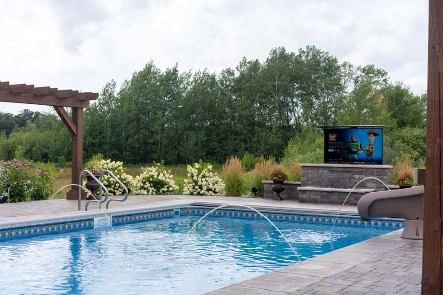 An outdoor TV mounted on a wall at the end of a pool. 