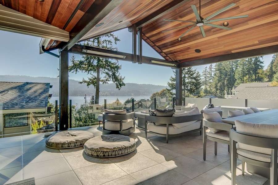 Covered outdoor patio with modern furniture, wood-paneled ceiling, and scenic lake view, designed for stylish outdoor living and entertaining.